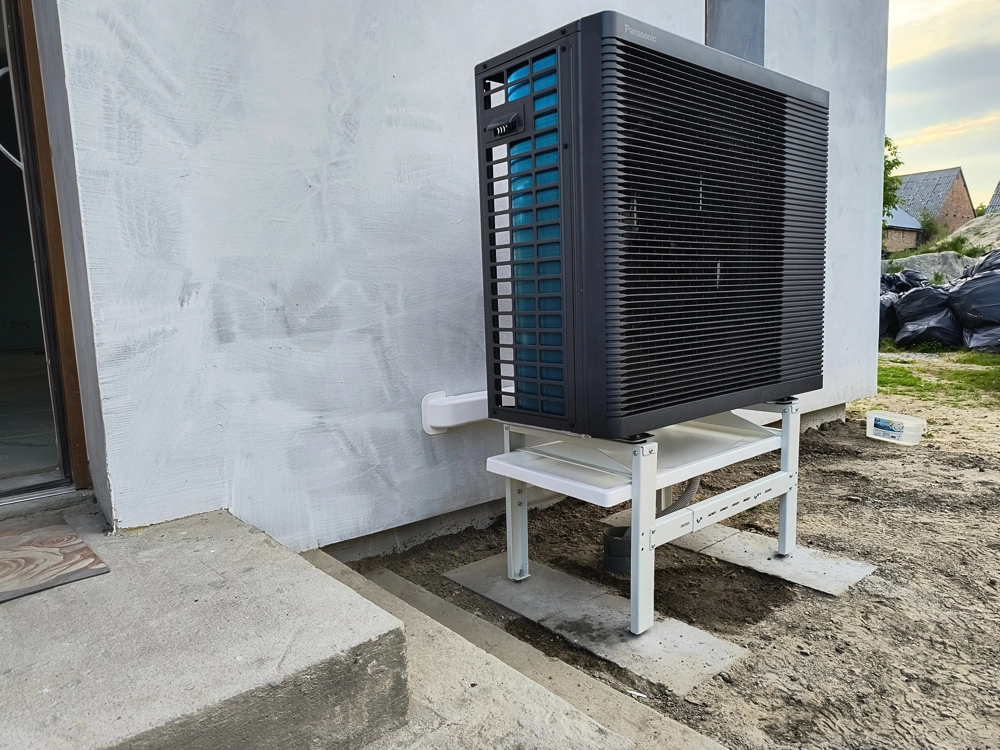 Zewnętrzna pompa ciepła zamontowana na białej konstrukcji wsporczej przy elewacji budynku Instalacja pompy ciepła