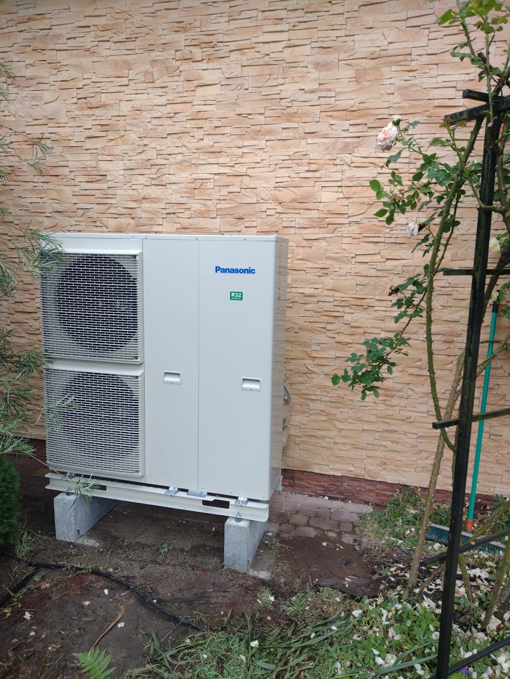 Zewnętrzna jednostka pompy ciepła powietrze woda zamontowana przy ścianie budynku na fundamentach