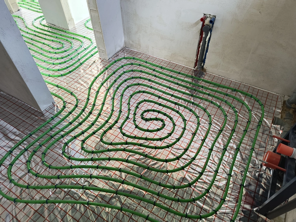 Ogrzewanie podłogowe – instalacja zielonych rurek na podkładzie izolacyjnym i metalowej siatce