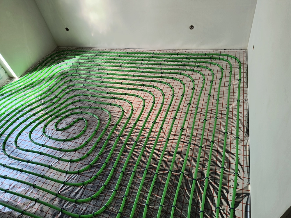 Ogrzewanie podłogowe: rozłożone na styropianie zielone przewody przed zalaniem wylewką