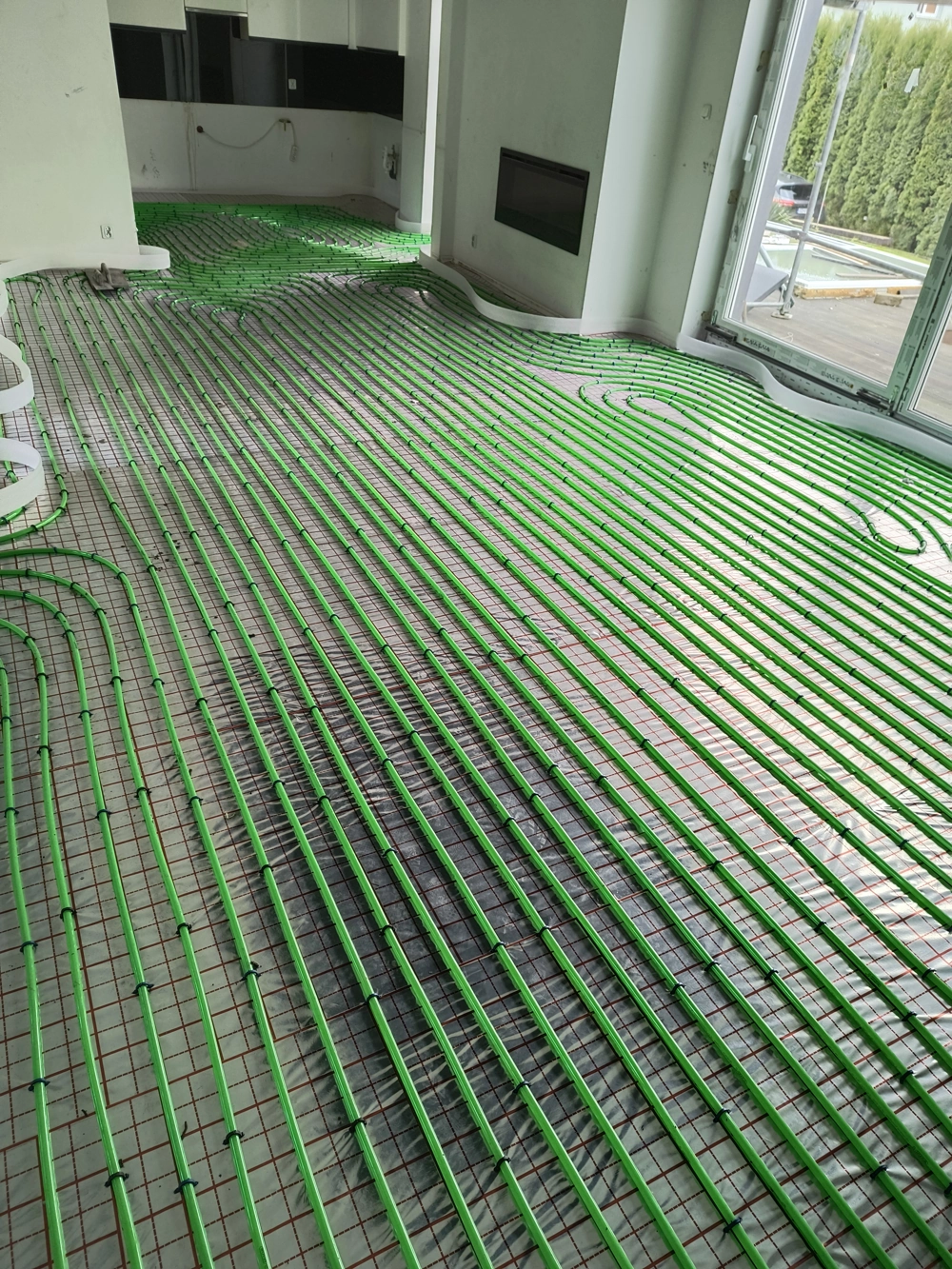 Zielone pętle rur ogrzewania podłogowego ułożone na siatce montażowej pod wylewkę w salonie